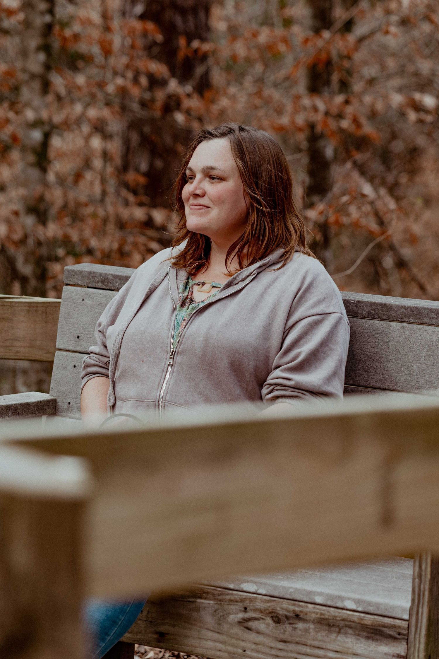 Person sitting on wooden bench during autumn outdoor photo session.