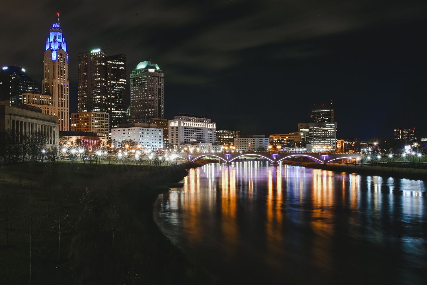 Baltimore Inner Harbor skyline illuminated at night with colorful reflections on the water.