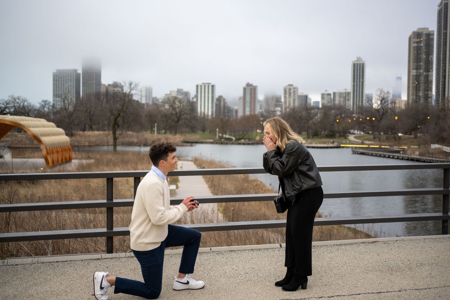 A couple shares a romantic marriage proposal moment on a bridge overlooking the city skyline.