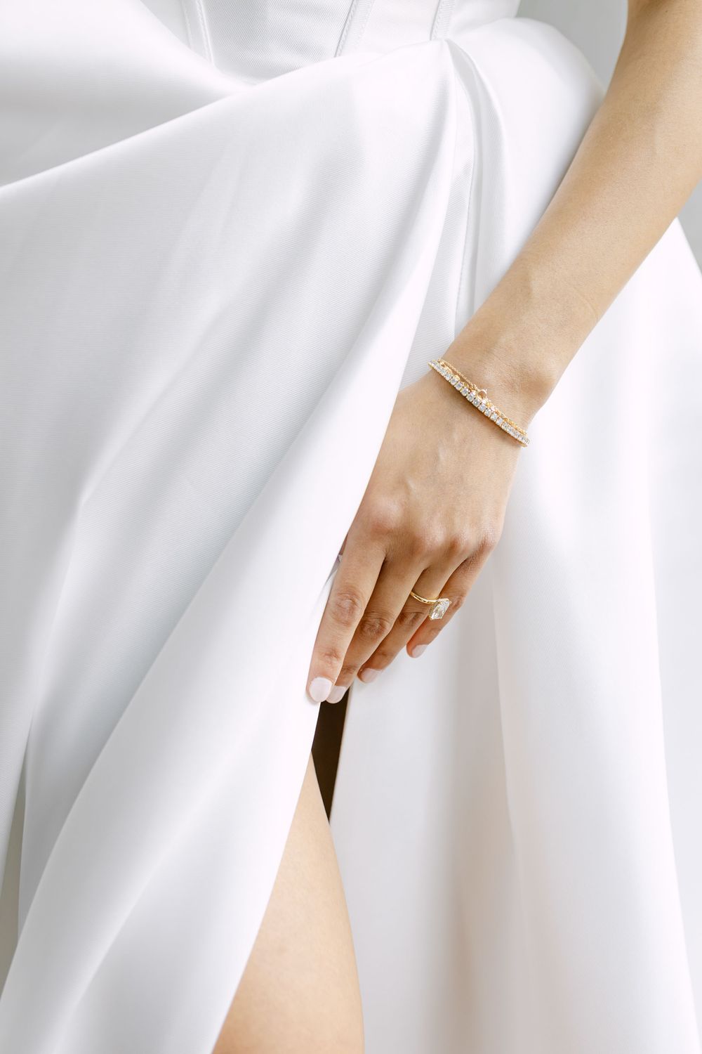 Close up of bride hand with engagement ring and bracelet holding wedding dress fabric in soft light