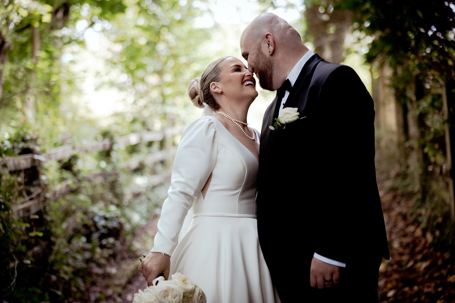 Bride and groom sharing an intimate moment in a lush forest setting, bride in elegant long-sleeve white gown.