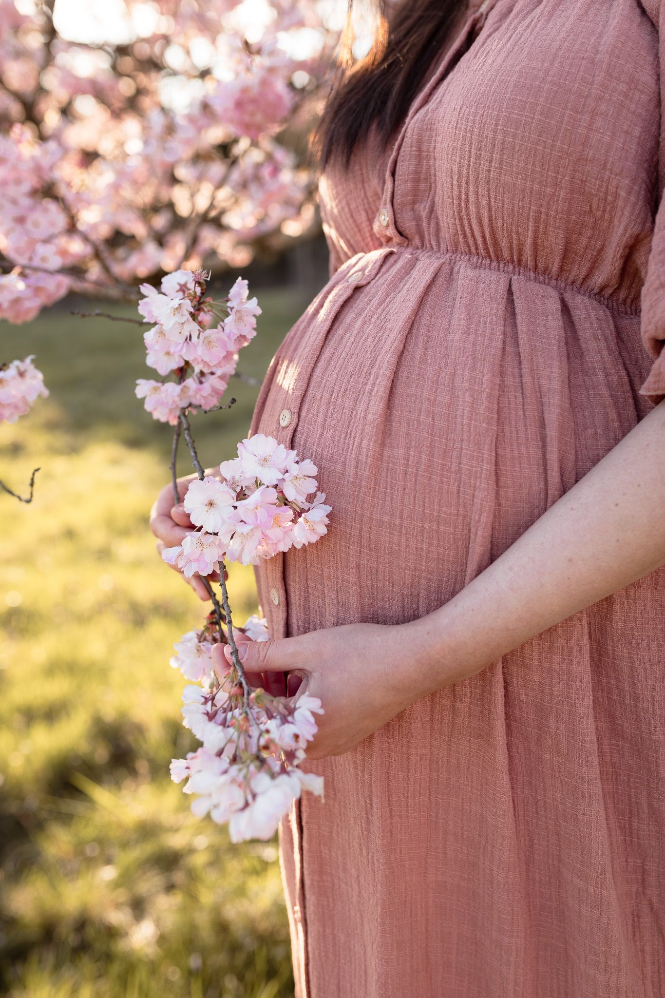 Robe de grossesse rose en gaze de coton suspendue devant un cerisier en fleurs pour séance photo maternité