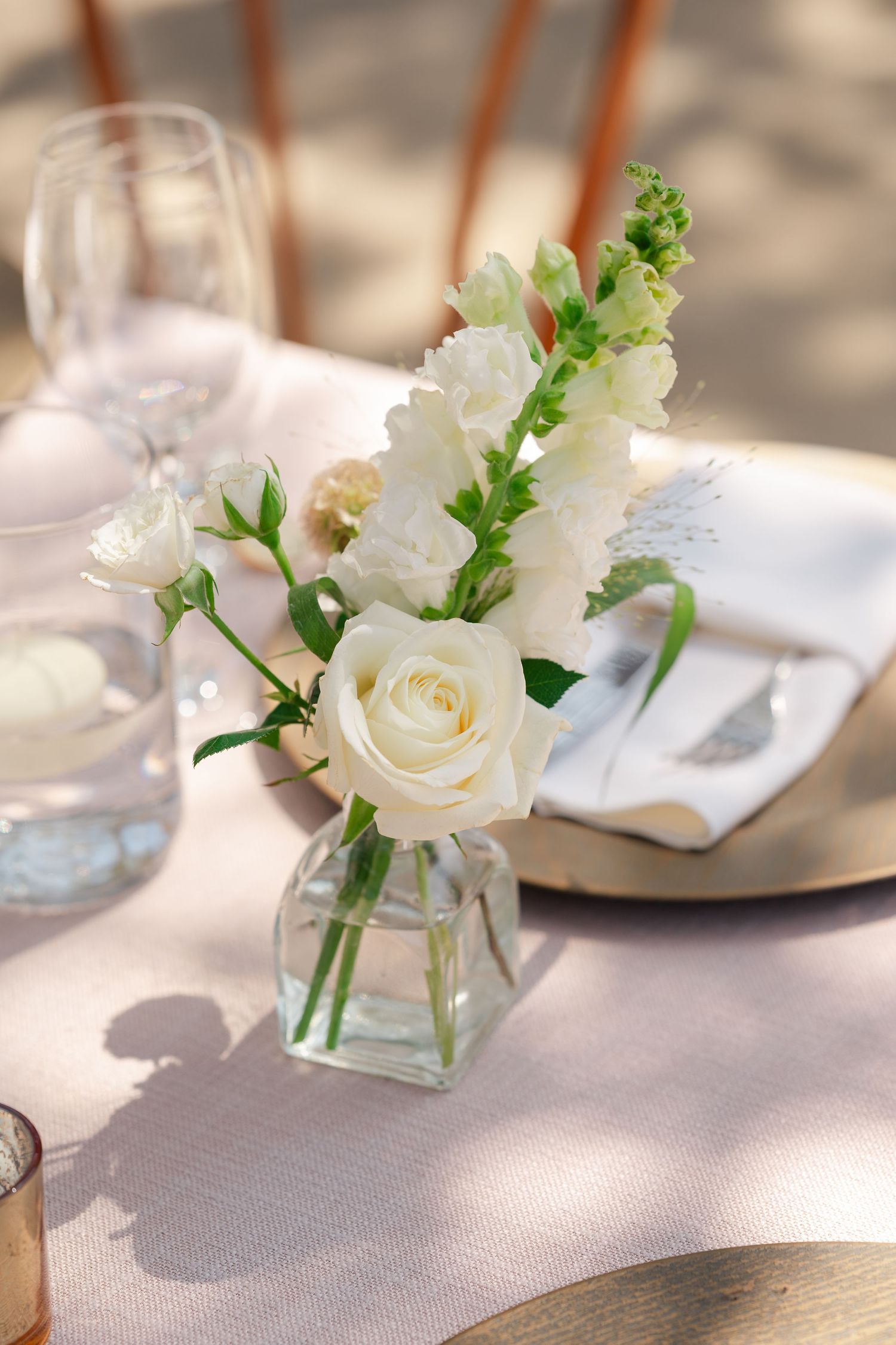 White roses and delicate greenery in small glass vases create an elegant table centerpiece setting.