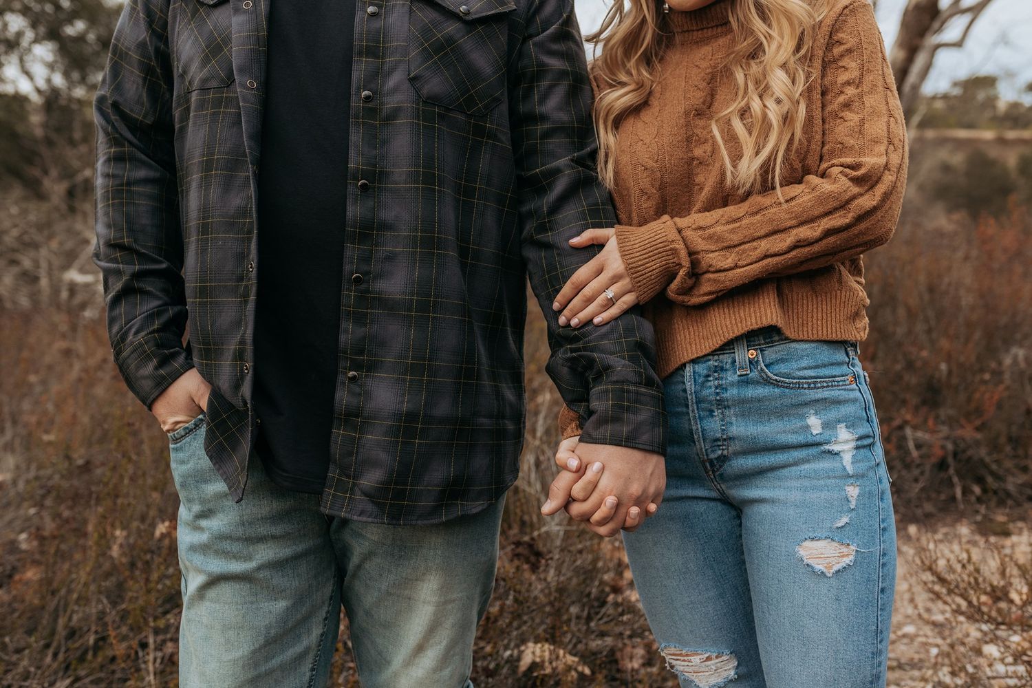 A couple in casual fall attire holding hands while walking through an autumn landscape at sunset in San Diego.