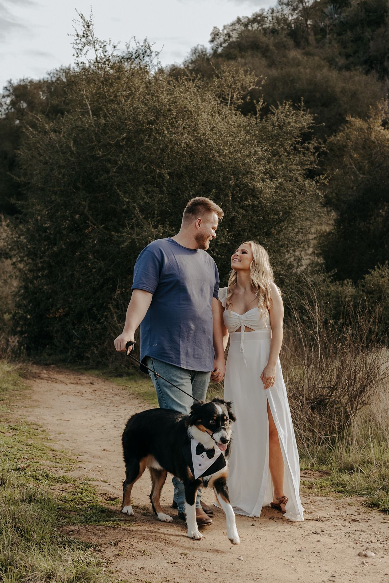 A couple walks their black and brown dog on a dirt trail surrounded by autumn foliage in San Diego.