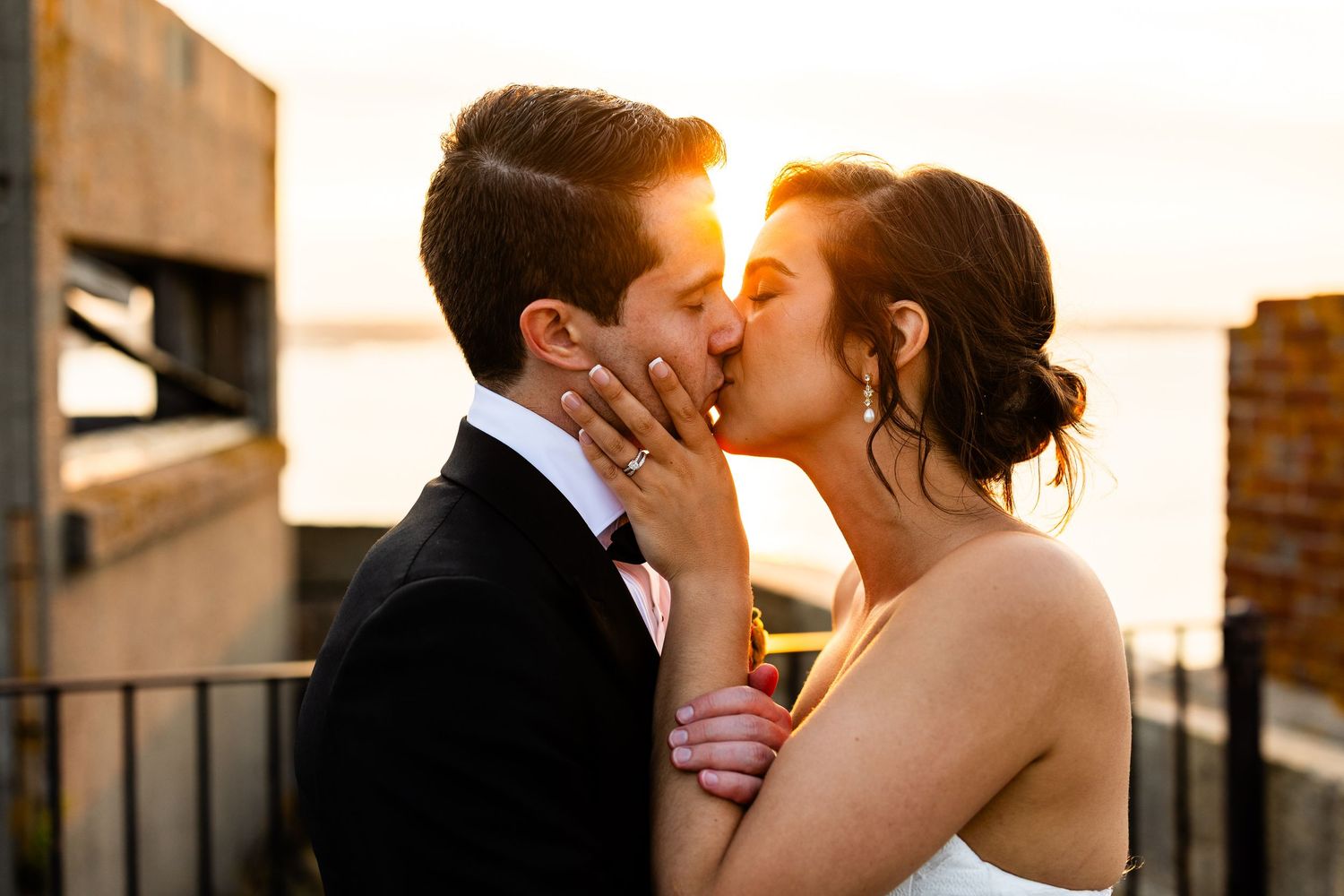Couple shares passionate kiss on rooftop balcony at golden hour.