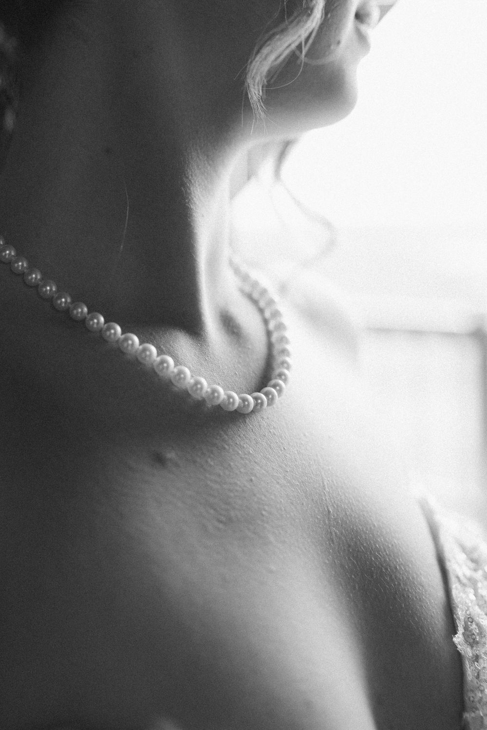 Artistic black and white close-up of a pearl necklace adorning someone's neck and collarbone.