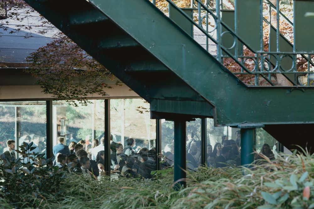 A row of modern apartment buildings with green balconies and railings set against a wooded backdrop.
