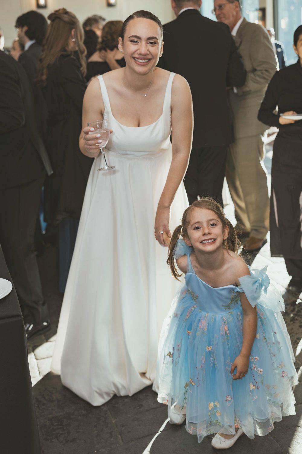 A woman in a white dress dances joyfully with a young child wearing a light blue dress at a wedding reception.