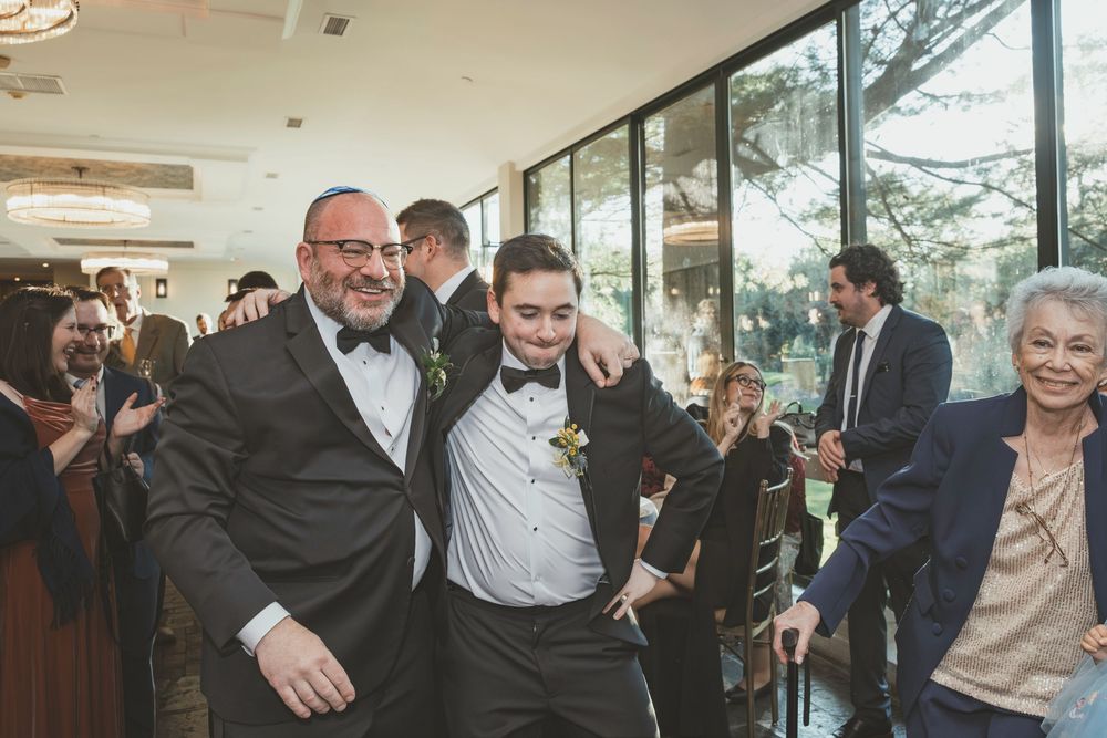 Wedding guests and party members celebrate in an elegant room with floor-to-ceiling windows.