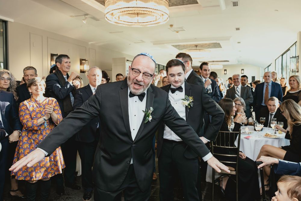 Wedding guests gather in an elegant reception hall with circular chandeliers and modern decor.