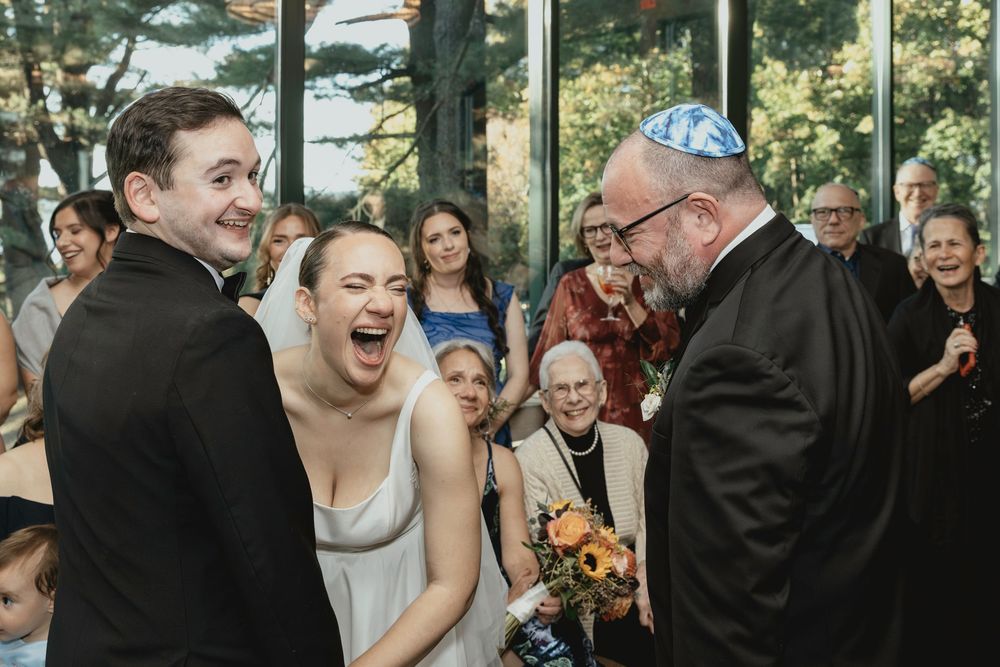 Wedding guests gather in a sunlit room with floor-to-ceiling windows during a celebration.