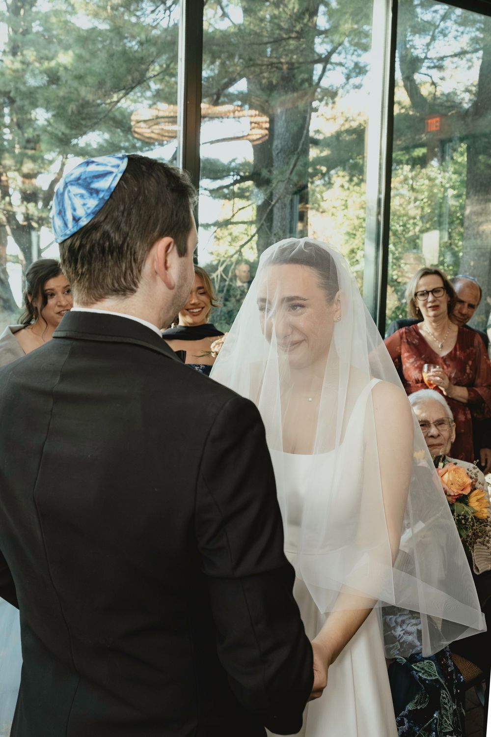 Wedding ceremony moment captured in bright indoor space with floor-to-ceiling windows.
