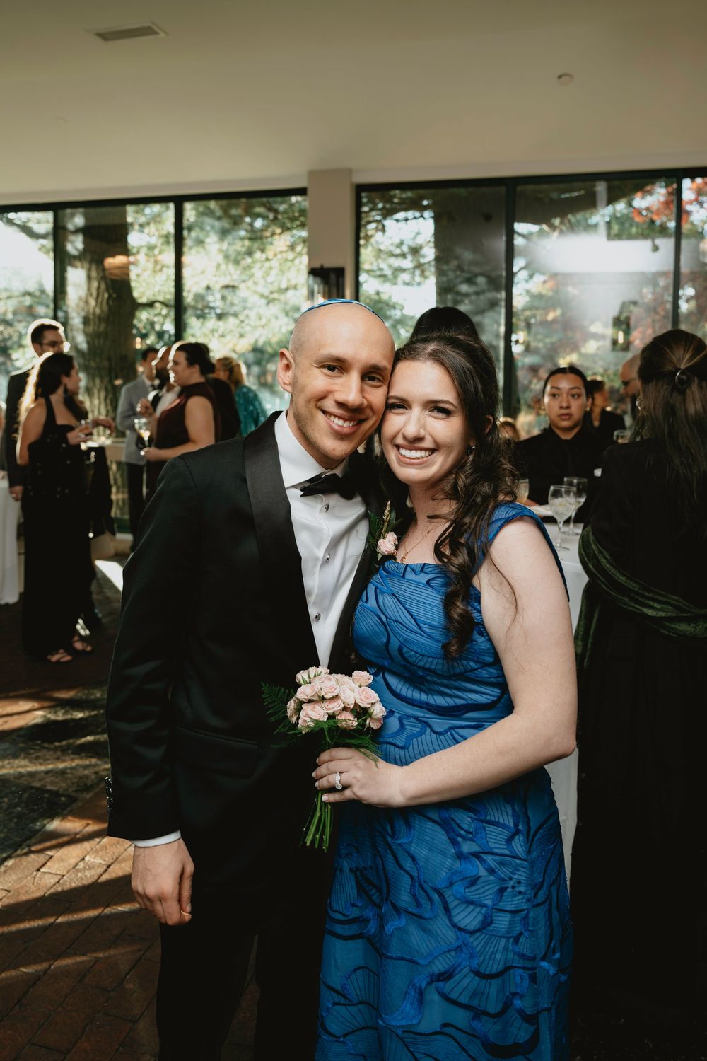 Wedding guests dancing and celebrating at an indoor reception with large windows and natural lighting.