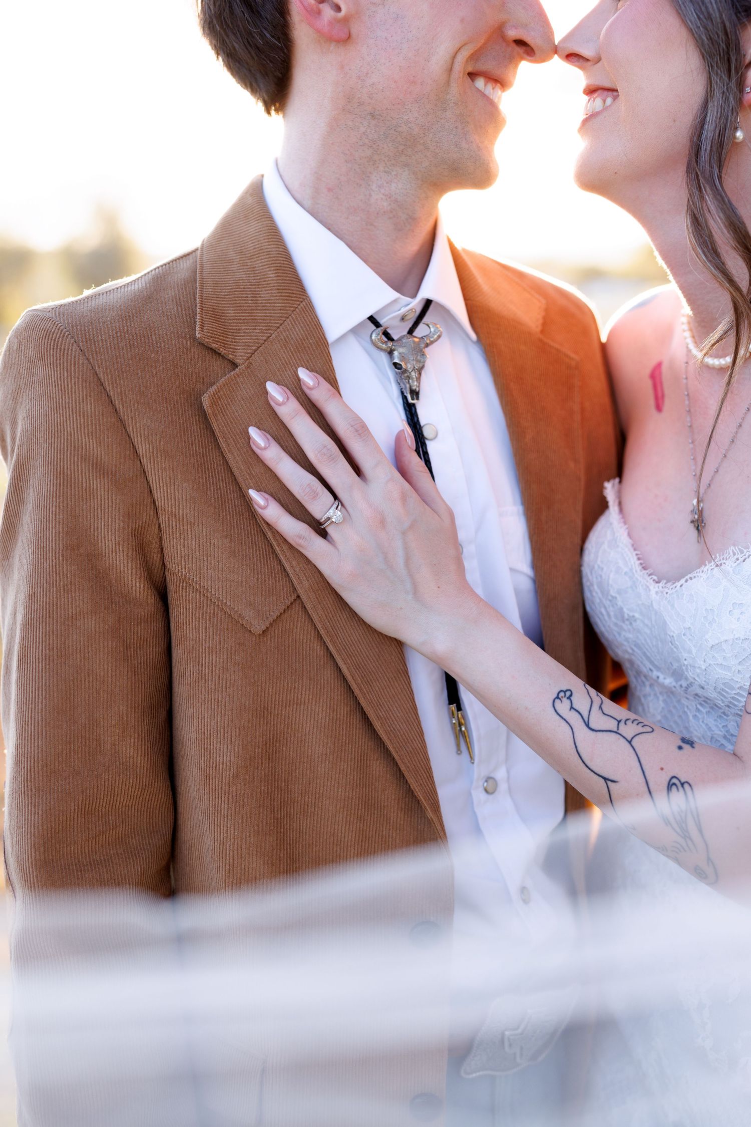 A tender wedding portrait showing a couple embracing, with the groom in a brown jacket and the bride in a white dress.