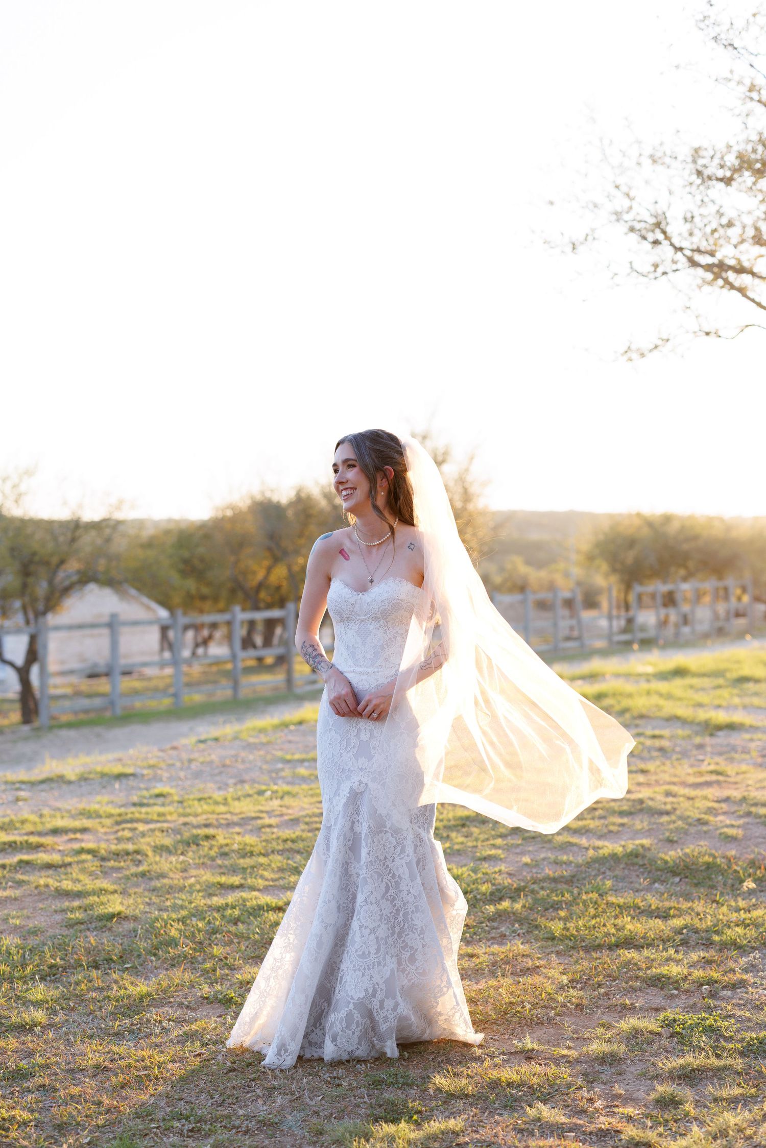 A delicate lace wedding gown catches the sunset light as the veil flows in the breeze.