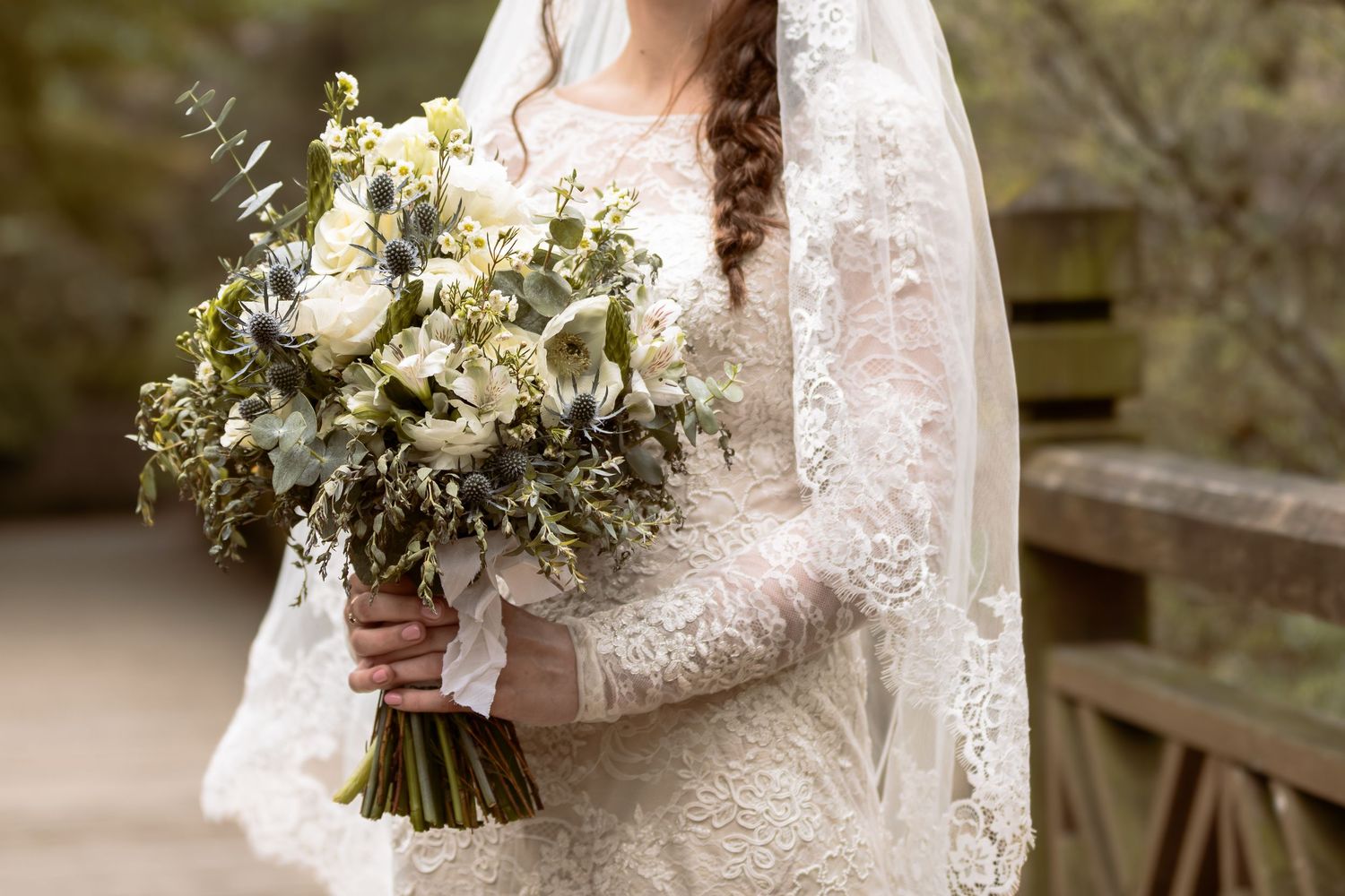 A beautiful white lace wedding dress with long sleeves and a stunning bouquet of white and green flowers.