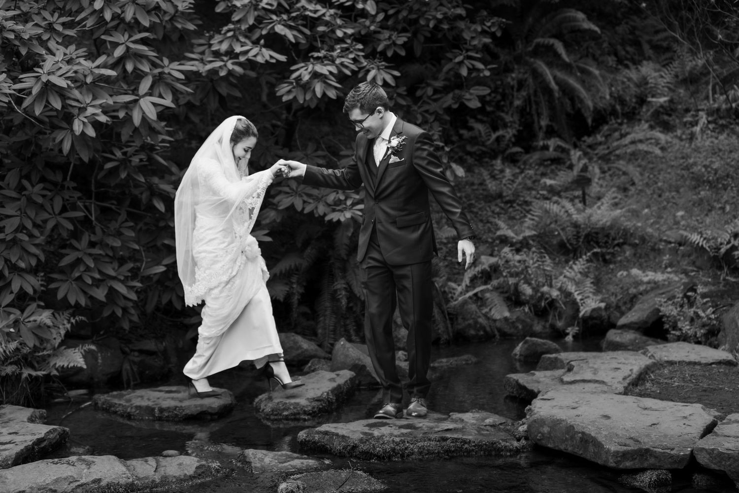 A person in white clothing crouches by a rocky stream in a lush forest setting.