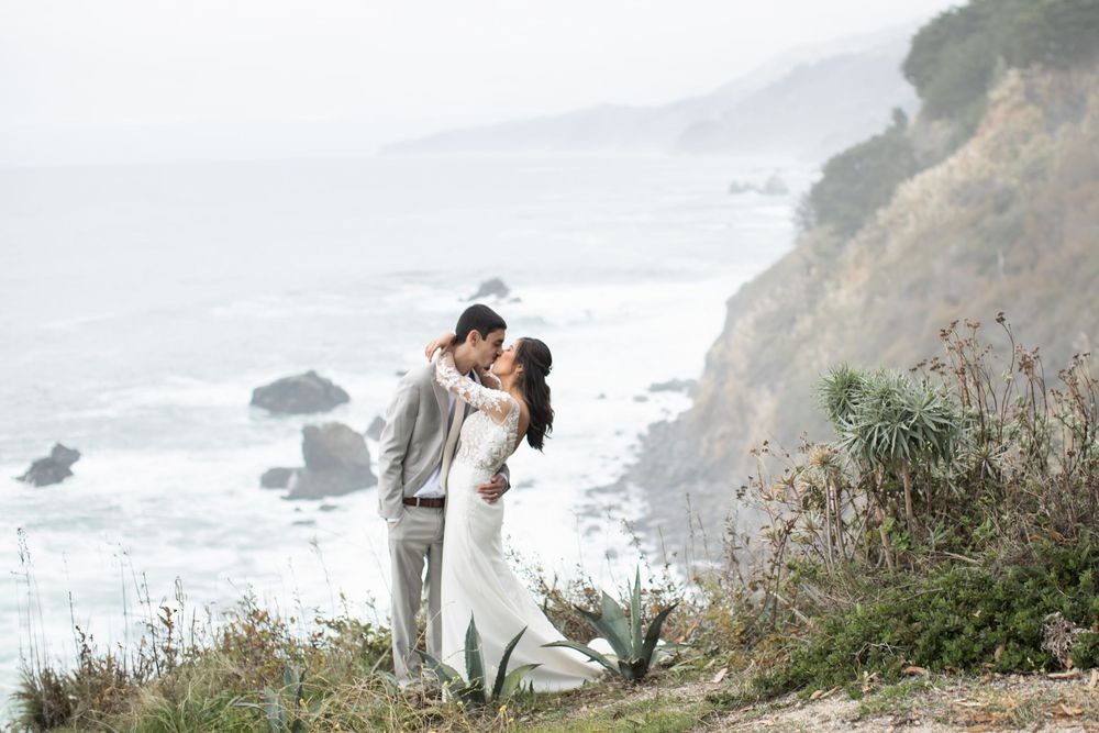 A couple shares a romantic moment on a scenic coastal cliff overlooking the misty Pacific Ocean.