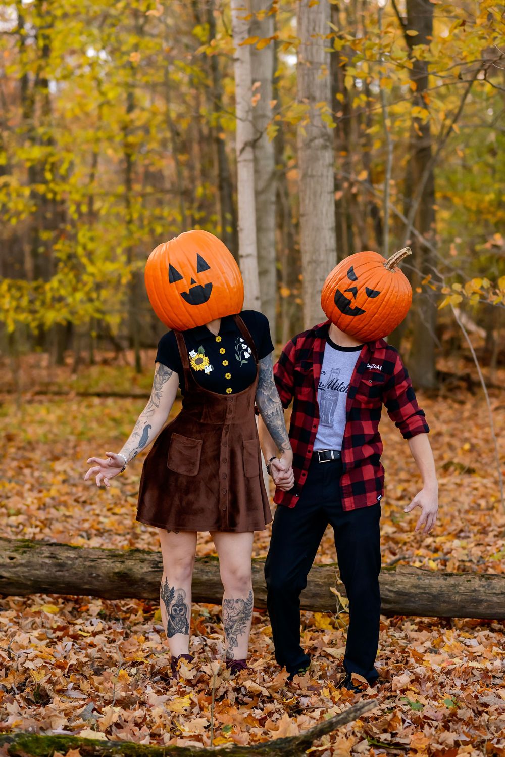 Couple wearing jack-o-lantern pumpkin heads holding hands in autumn forest with fallen leaves at Komoka Provincial Park.