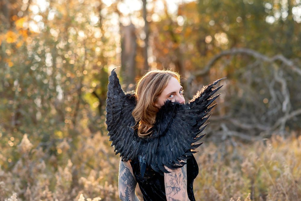 Woman with long red hair wearing black angel wings poses in an autumn forest setting at Komoka Provincial Park.