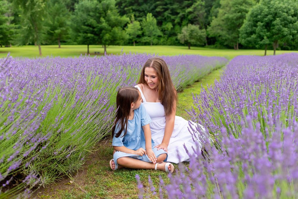 Mother and daughter sitting together in a blooming purple lavender field surrounded by green trees.