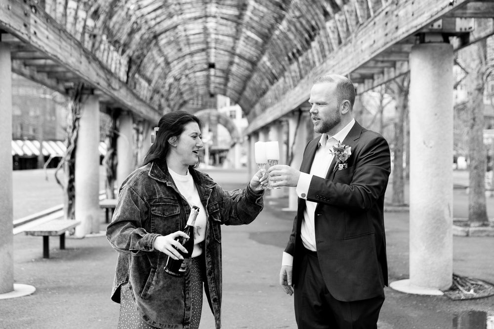 A couple toasting drinks under an arched pergola in a black and white outdoor photo.