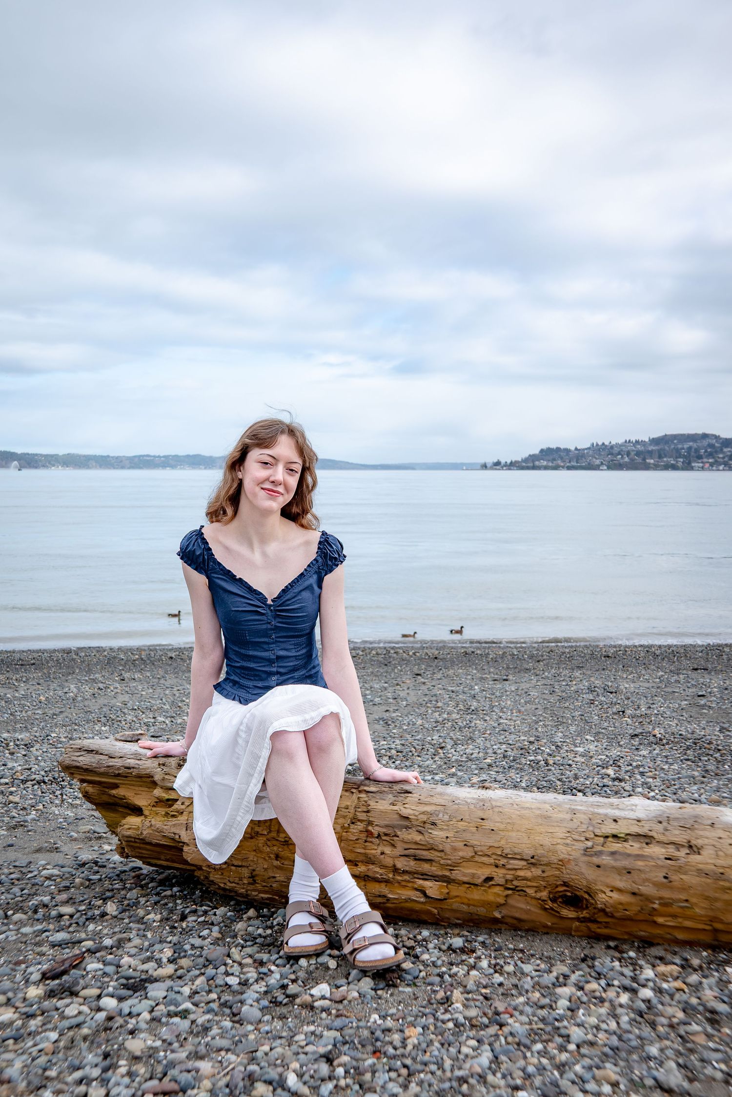 Senior sitting on driftwood at Tacoma waterfront beach for graduation photos.