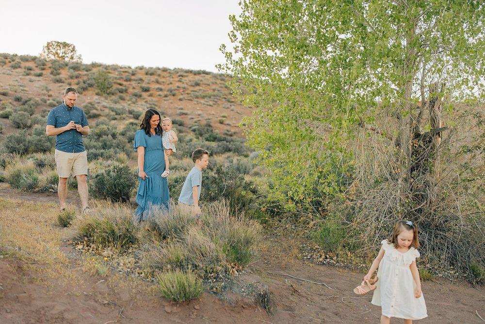 Family of four enjoying a scenic desert hillside with lush green trees and sagebrush during golden hour.