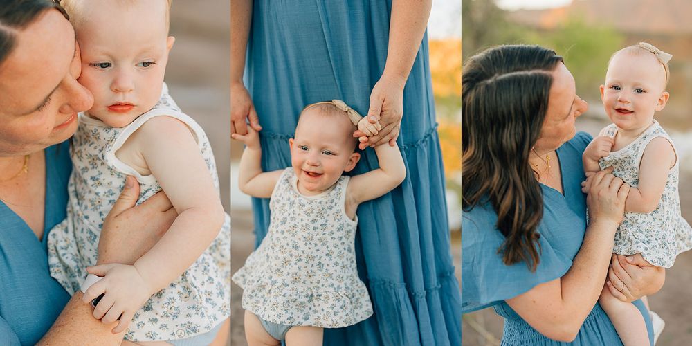 Mother holding smiling baby girl in floral dress outdoors, with blue dress and desert landscape backdrop.