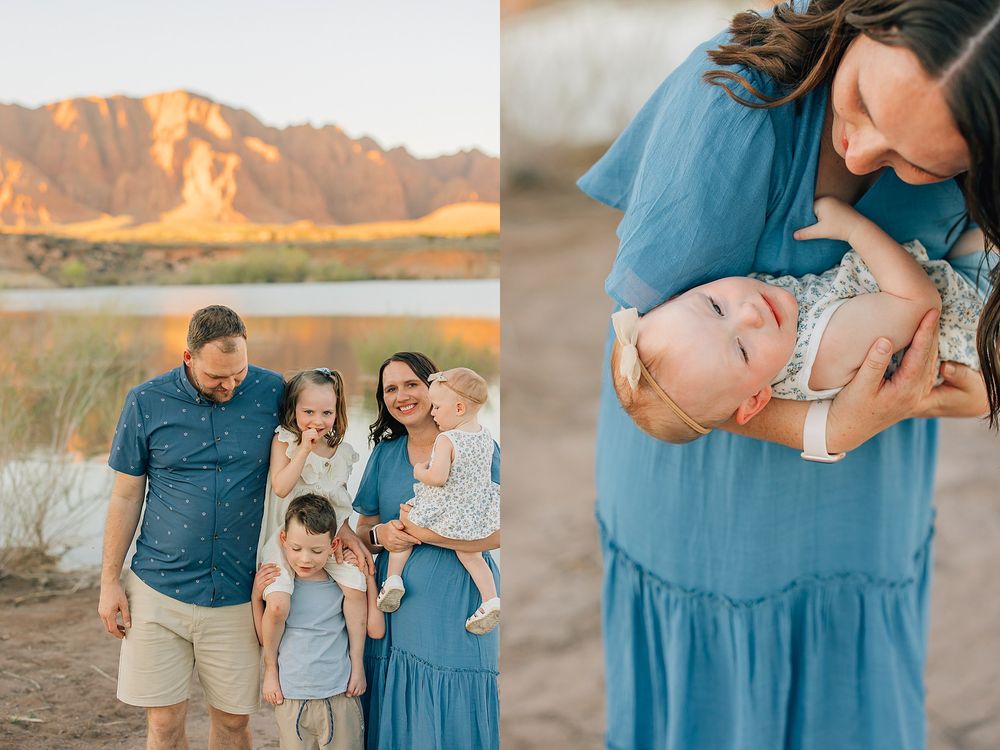Family portrait session at golden hour near a lake with mountains, mother holding smiling baby in blue dress outdoors.