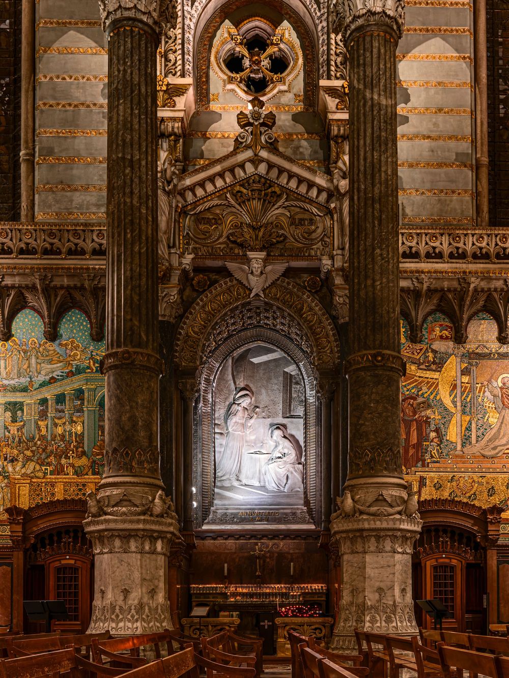Ornate cathedral interior with gilded arches, marble columns, and illuminated Pieta sculpture in decorative Gothic niche.