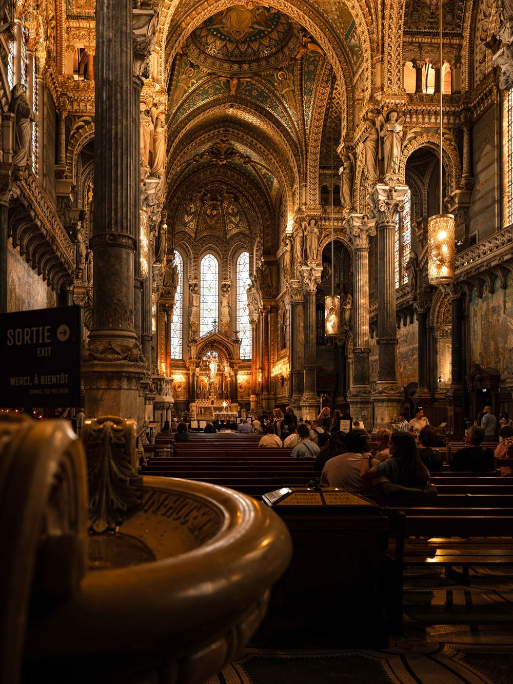 Ornate cathedral interior with golden arches, mosaic ceilings, and glowing altar in Lyon, France.