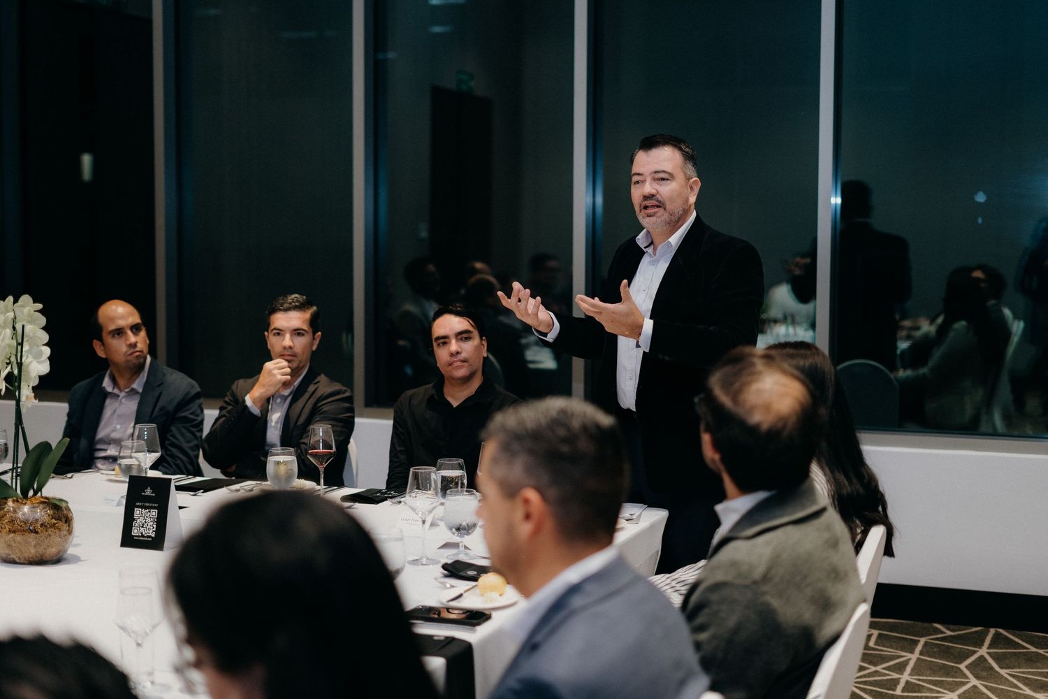 Business professionals gathered at a formal dinner meeting in a modern conference room setting.