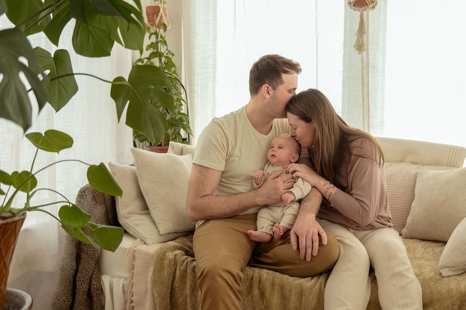 A couple shares a romantic moment together on a beige couch in a bright living room with houseplants.
