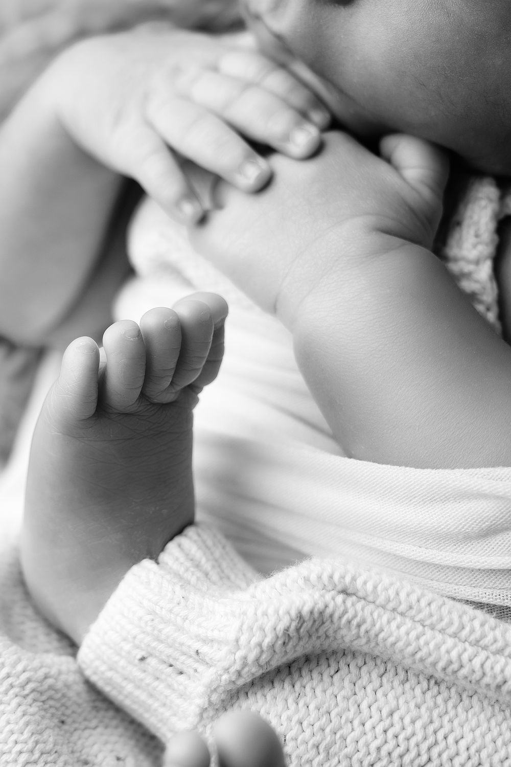 Black and white close-up photo of tiny newborn baby feet wrapped in soft white knitted blanket.
