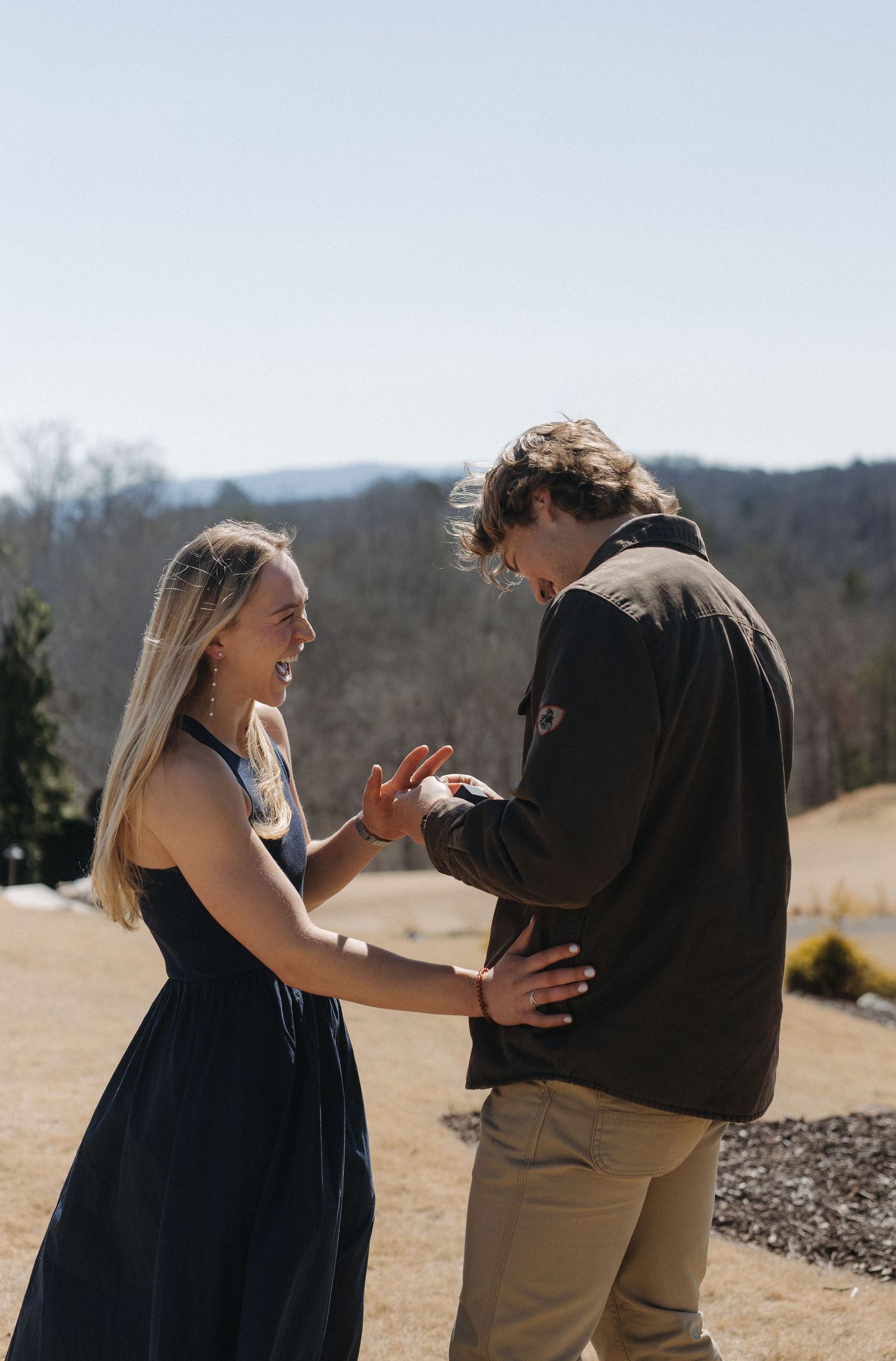 A couple shares a joyful moment together on a sunny hilltop with mountains visible in the background.