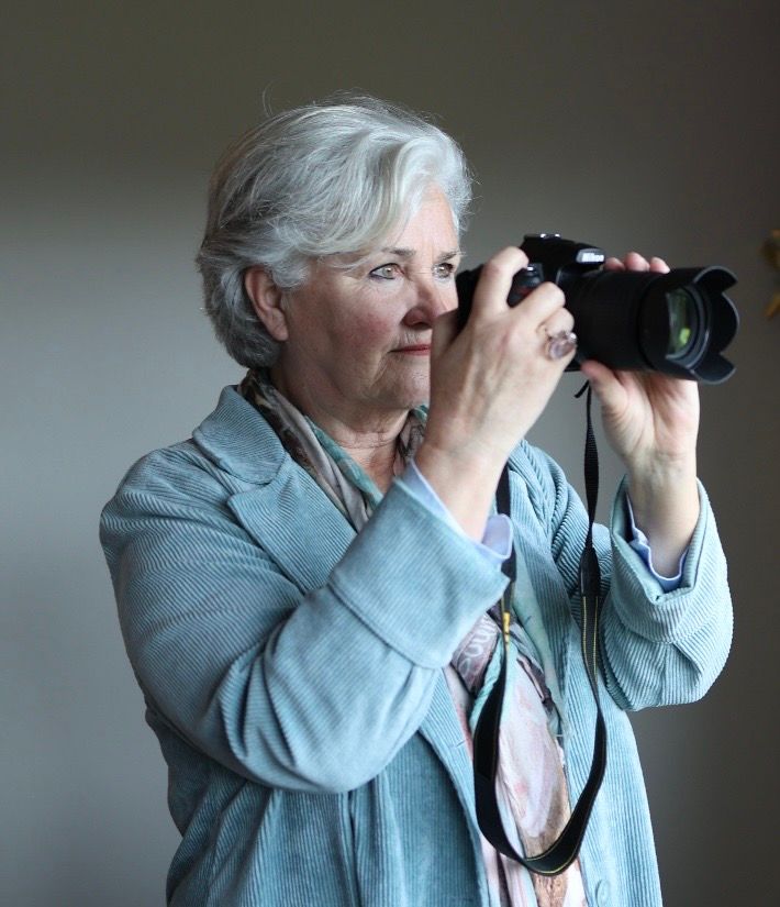 Senior woman with white hair photographing with a professional DSLR camera in a softly lit studio.