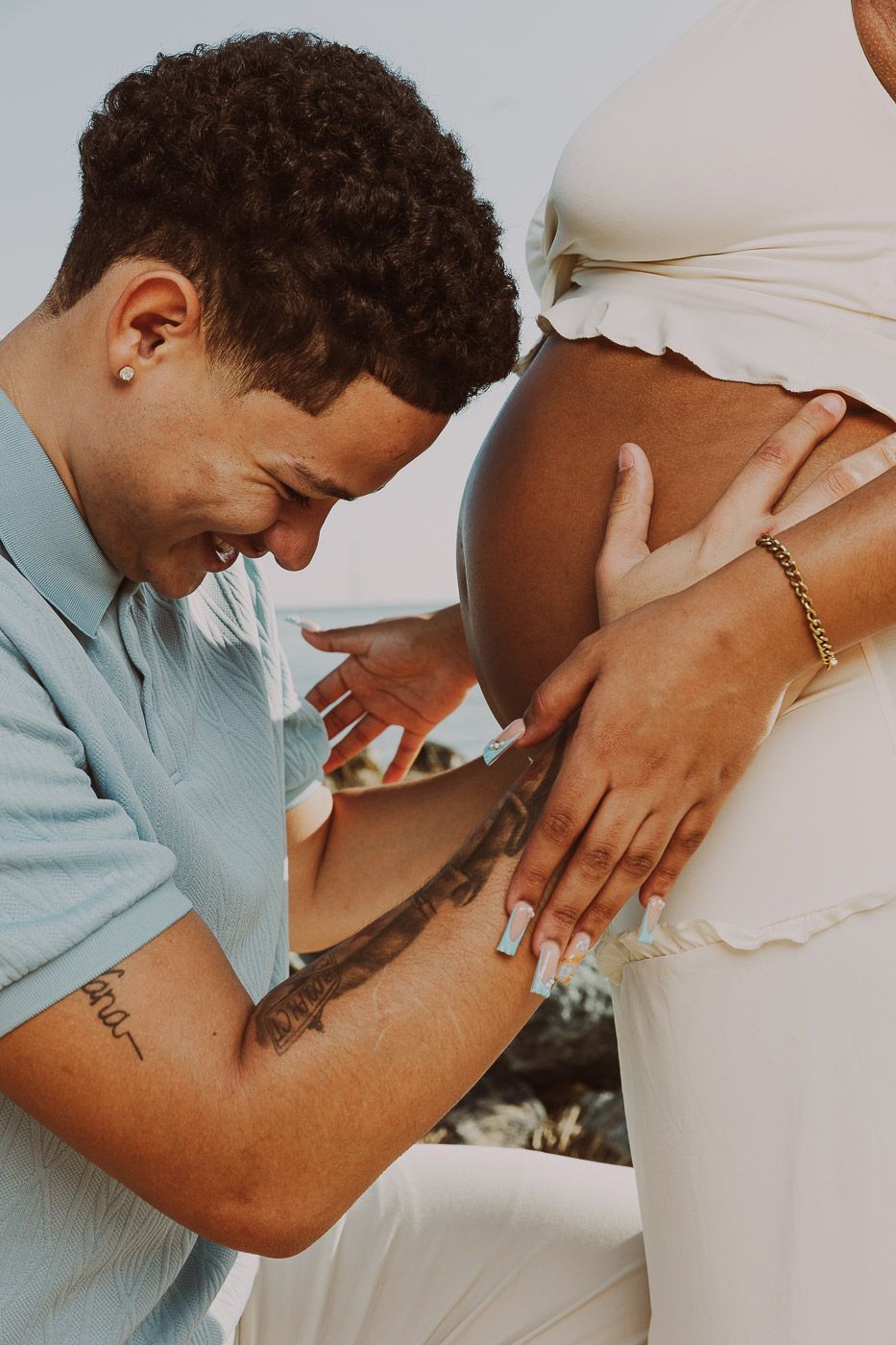 Loving partner leaning down to kiss pregnant woman's baby bump outdoors in a tender maternity photo session.