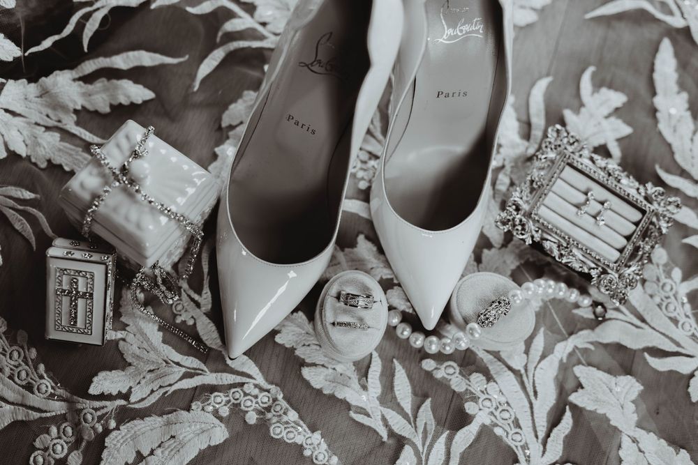 Christian Louboutin white heels with pearl jewelry and perfume on lace fabric for a wedding flat lay.