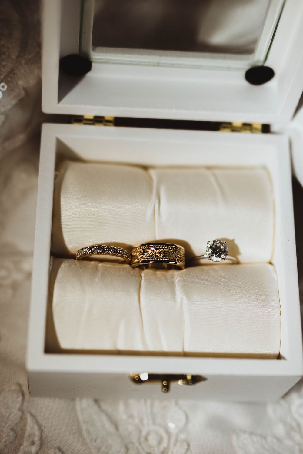 Gold wedding bands and diamond engagement ring displayed in a white velvet jewelry box.