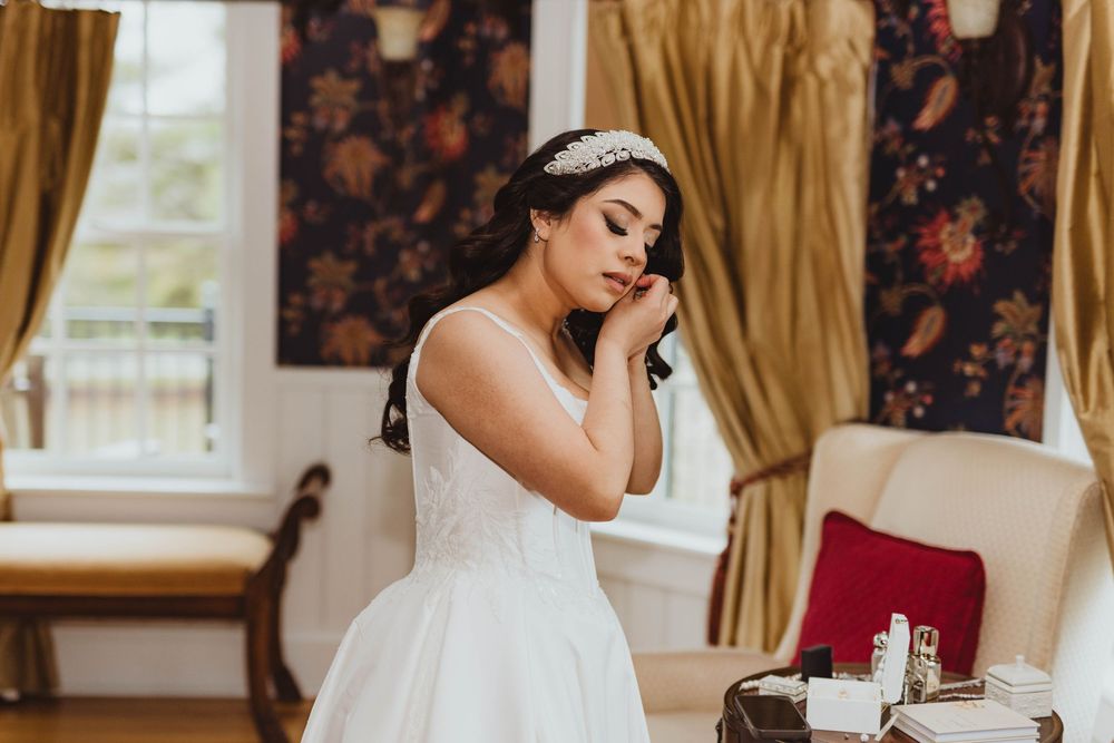 Emotional bride in white ball gown and pearl headpiece touching her face while getting ready.