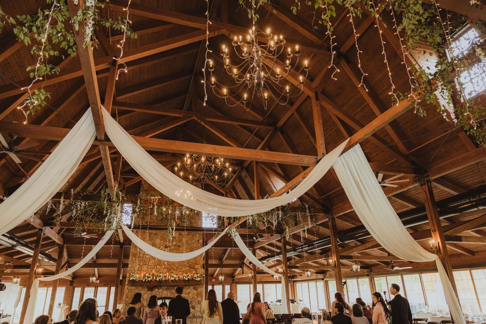 Rustic barn wedding reception venue decorated with white draping, greenery, and warm chandelier lighting.