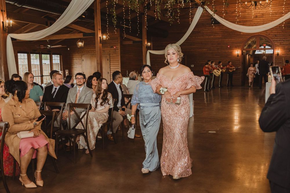 Two elegantly dressed women in lace gowns walking down the aisle at a rustic barn wedding.