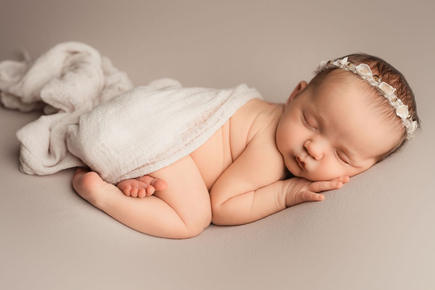 Sleeping newborn baby in cozy beige knit outfit and bear hat resting on fluffy tan blanket.