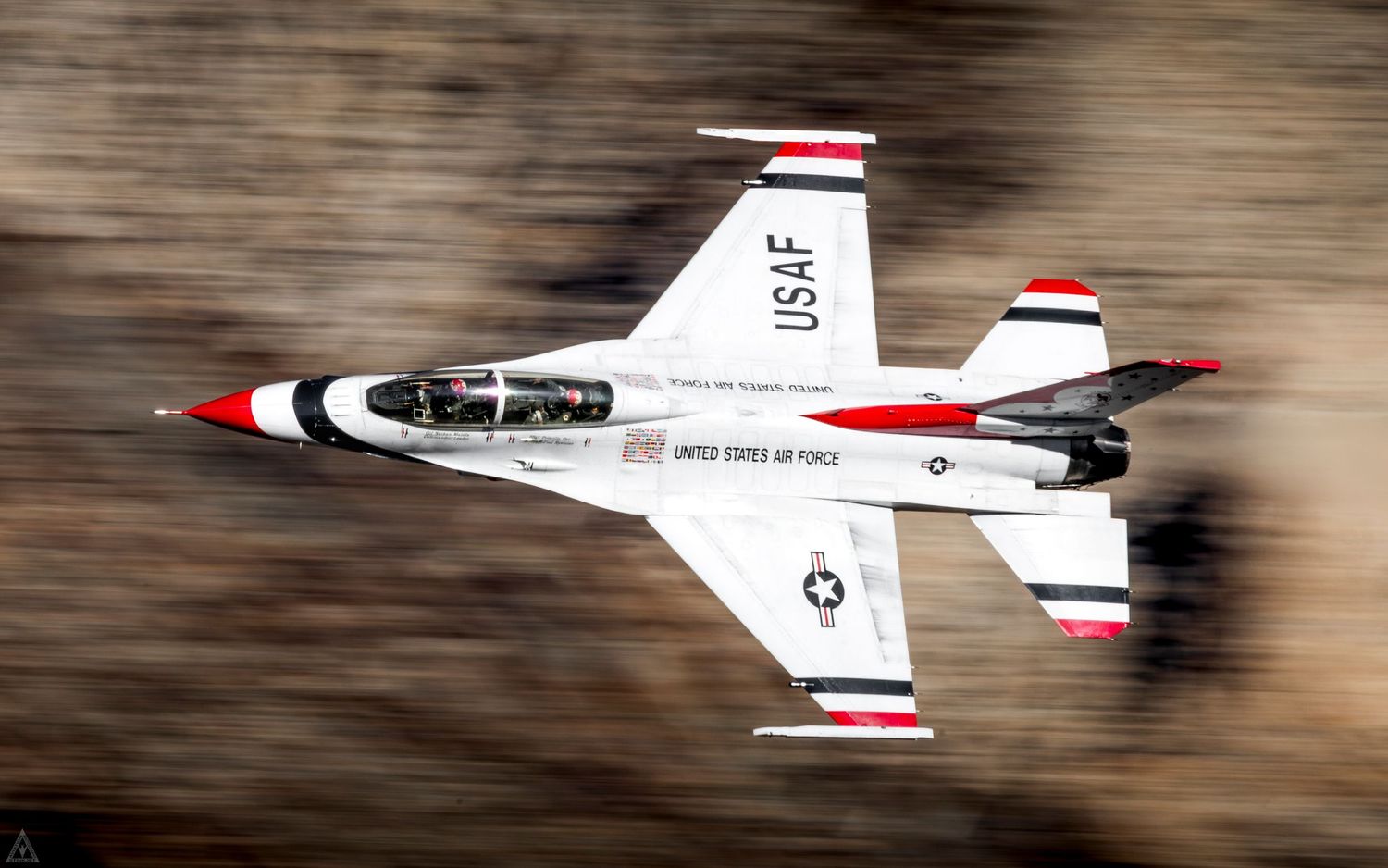 A Thunderbird F-16 flying at great speed through a desert canyon