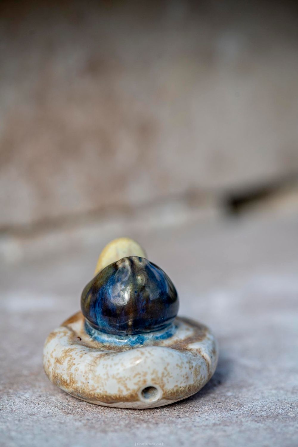 Close-up of a small ceramic figurine with blue and gold glaze sitting on a round pottery base.