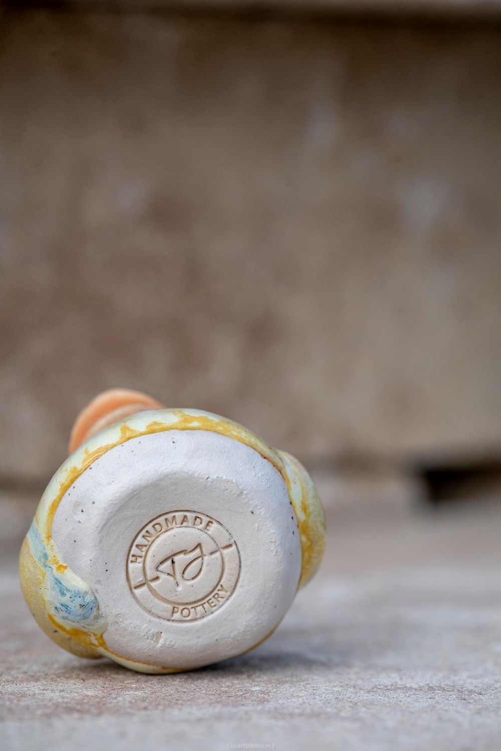 Bottom of a handmade pottery ceramic vase showing embossed maker mark stamp on white unglazed base.