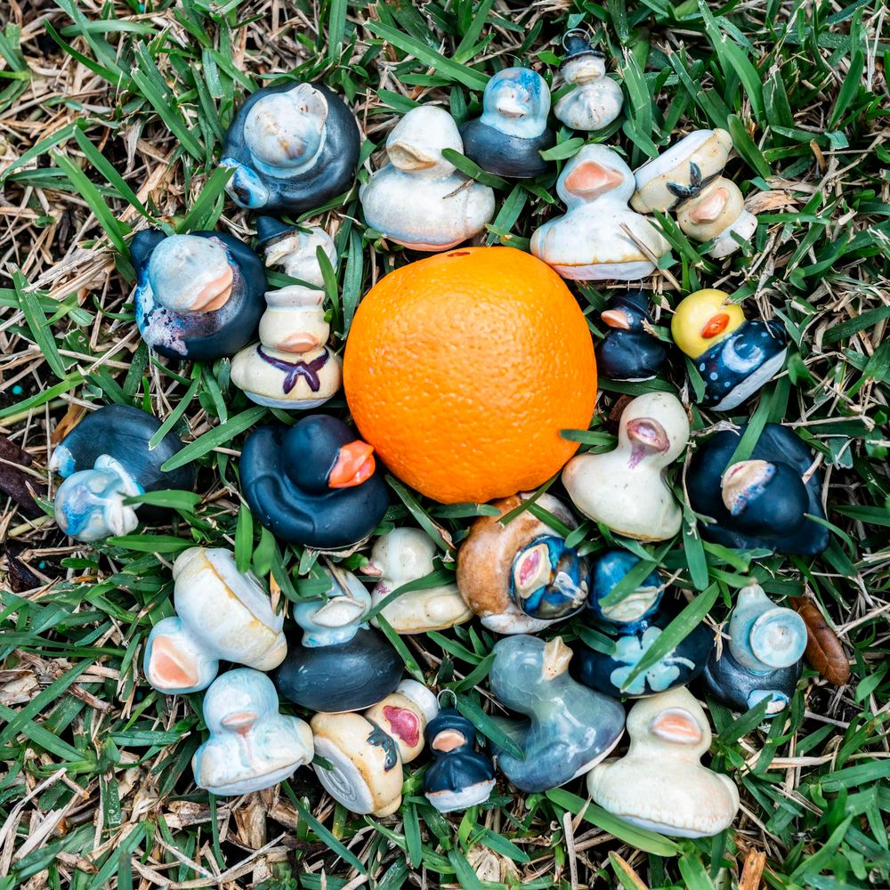 Colorful handmade ceramic animal figurines arranged in a circle around a fresh orange on green grass.