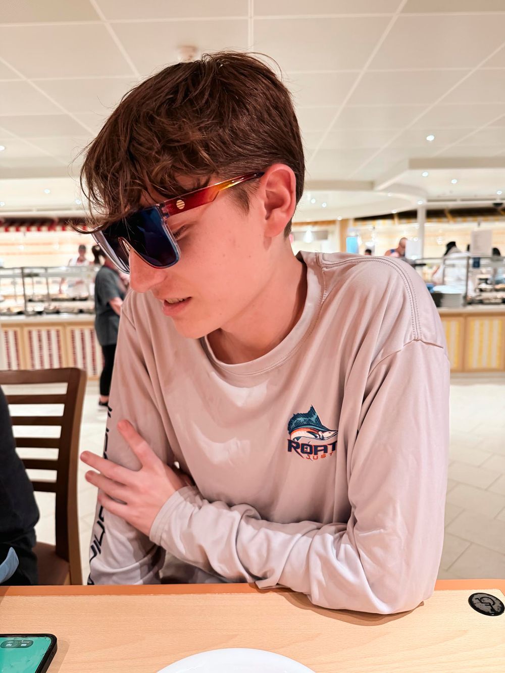 Young man wearing sunglasses and a beige long-sleeve fishing shirt sitting at a restaurant table.